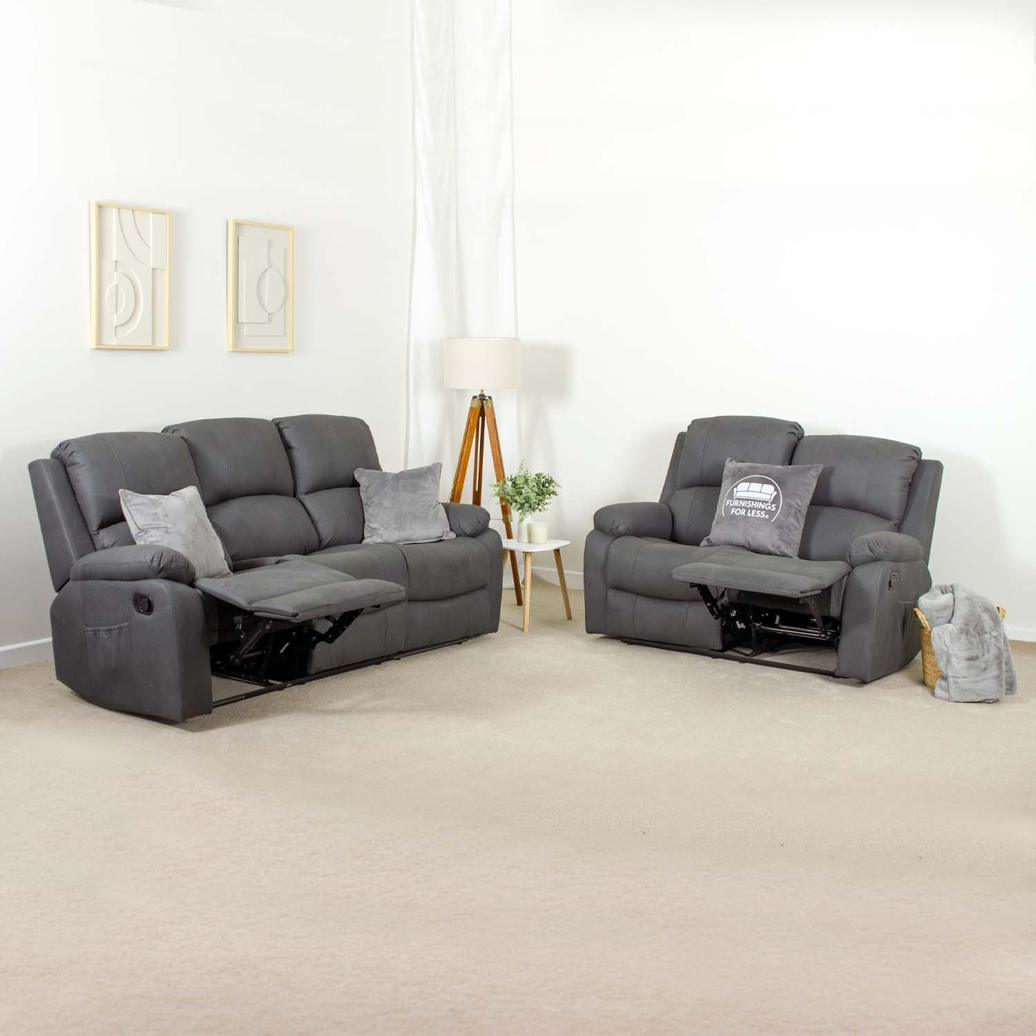 A dark gray reclining sofa and matching armchair set with gray throw pillows, shown in a minimalist white room with beige carpeting.